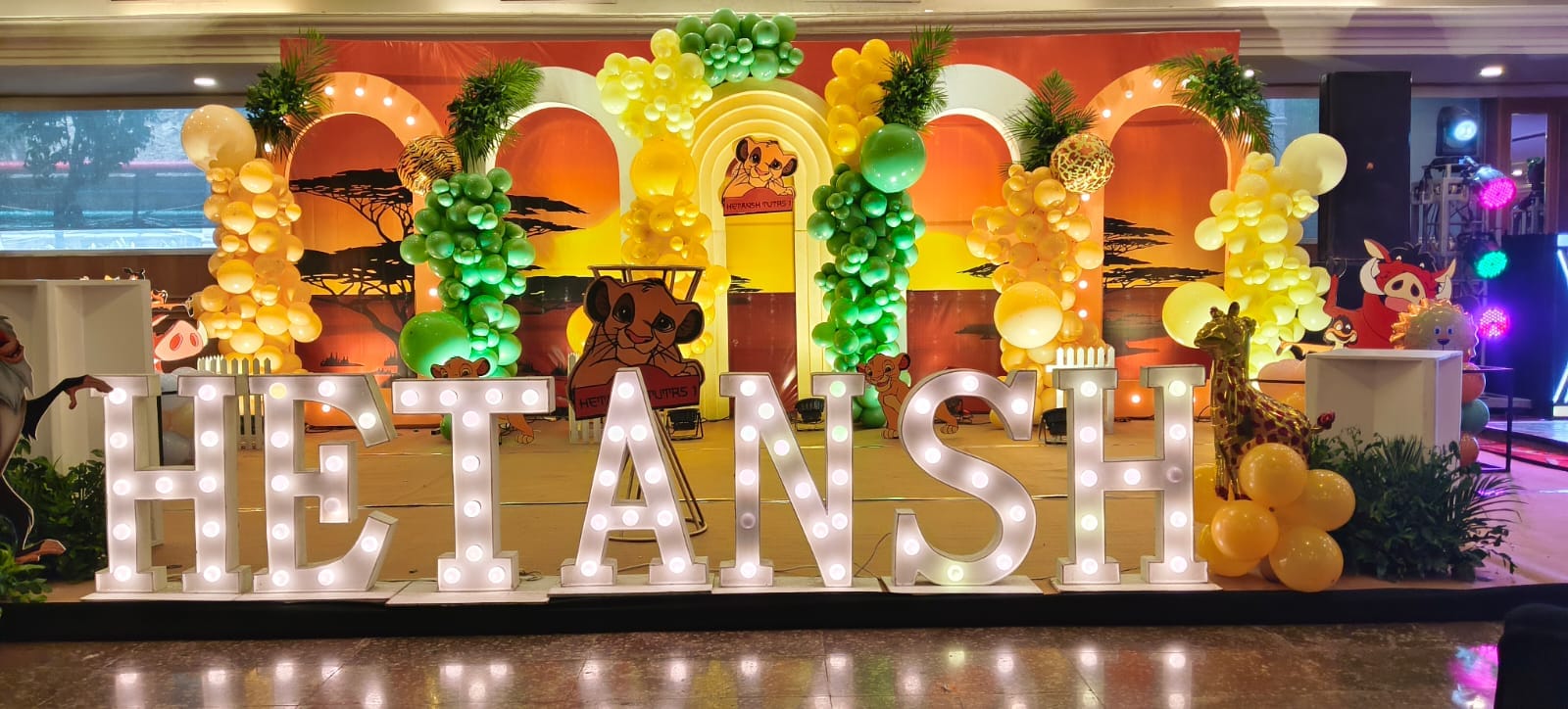 A colourful birthday stage with balloon arches and illuminated lettering