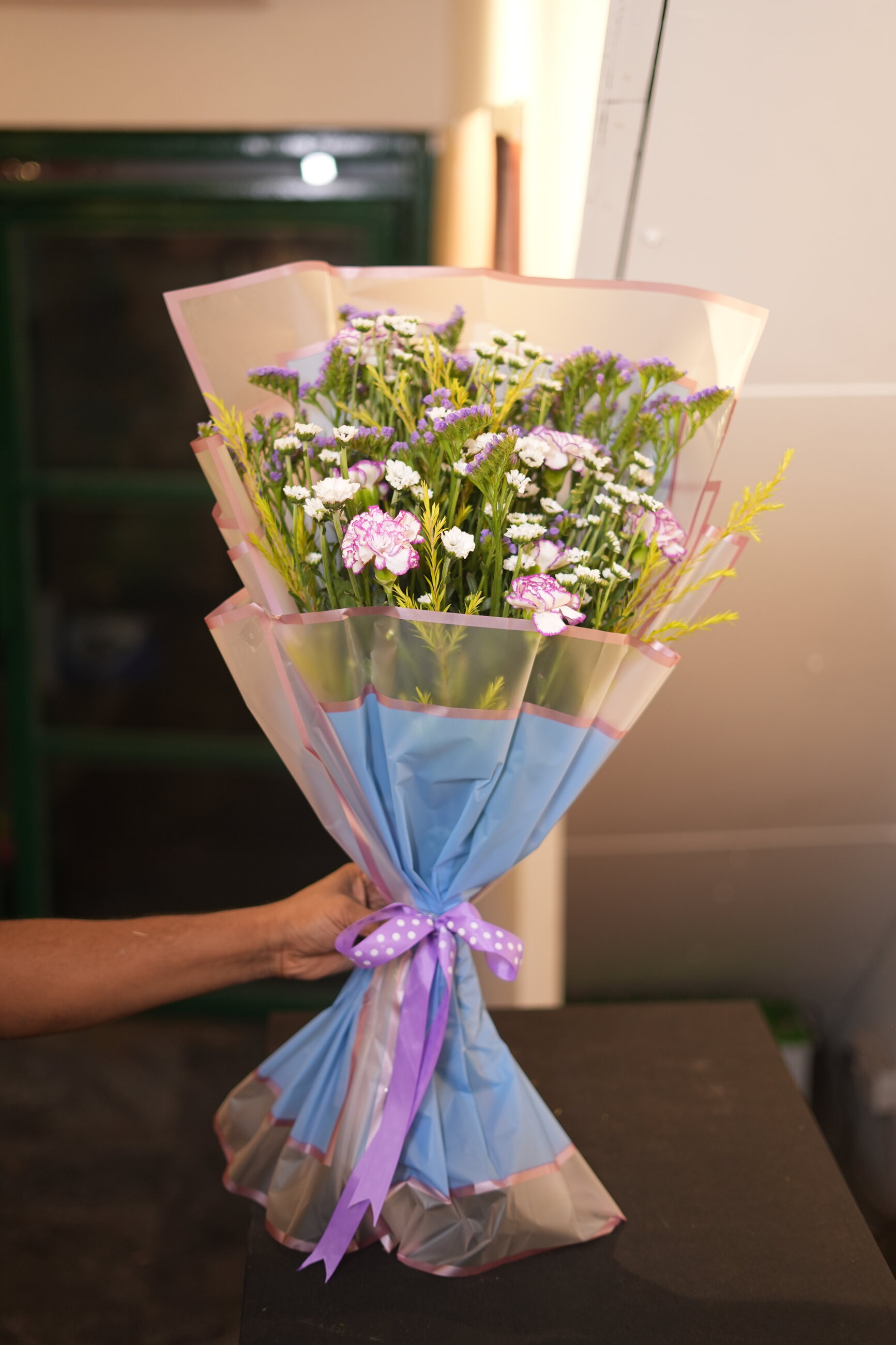 A pastel bouquet wrapped in tissue with a lavender ribbon
